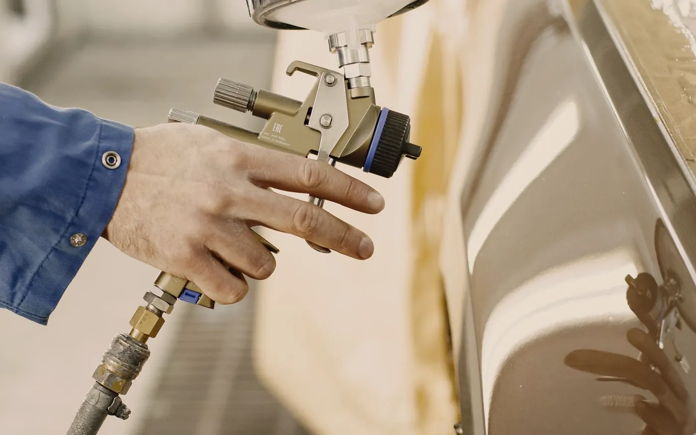 Spray gun applying paint to a car body panel in a workshop