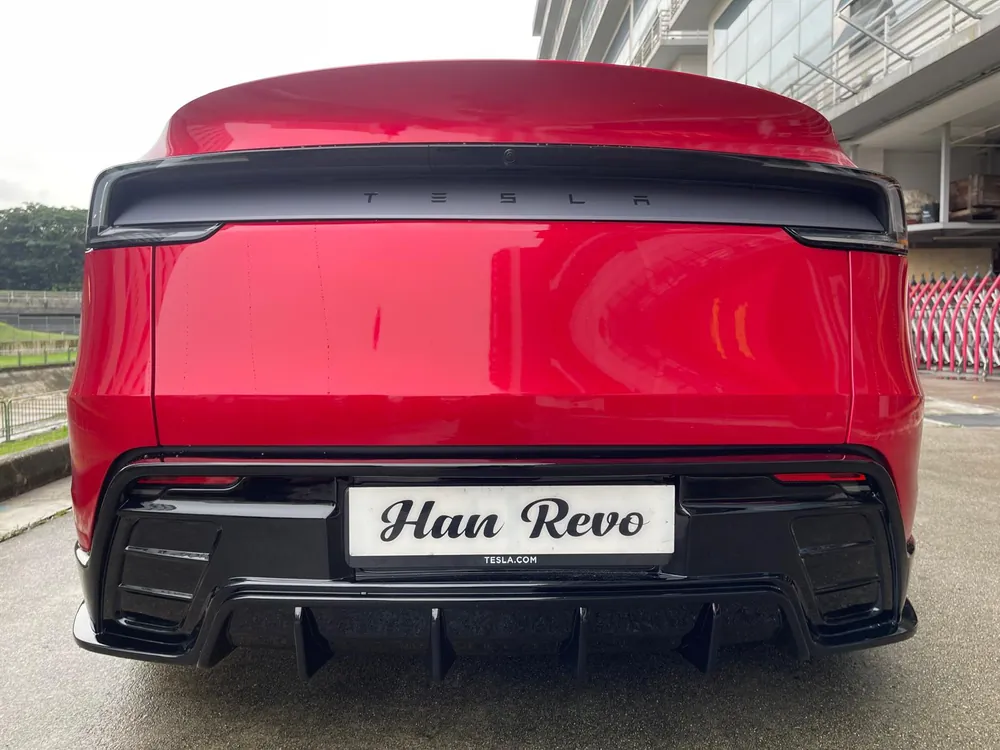 Rear three-quarter view of the rev 1 bodykit with boot spoiler on a red Model Y Juniper