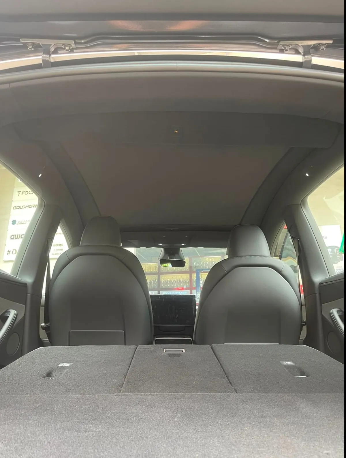 Electric auto roof shade closed across the glass roof of a Tesla Model Y Juniper, seen from the boot with the rear seats folded